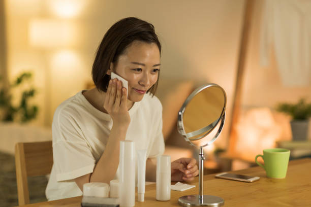 A woman applying skincare products while looking in a mirror at home.