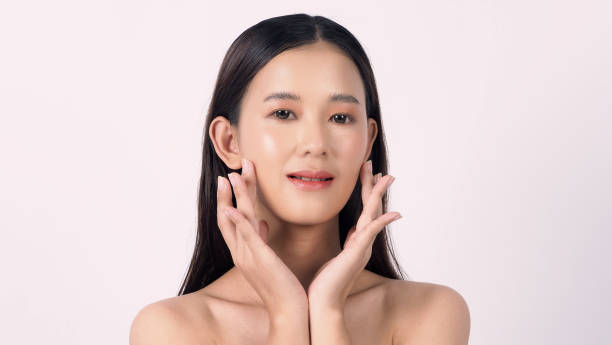 Portrait of a young Asian woman with clear skin touching her face gently on a white background